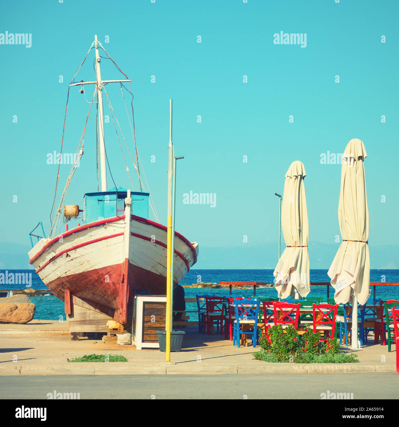 Old fishing boat and street cafe on the seashoe, Aegina,  Greece. Vintage style toned image Stock Photo