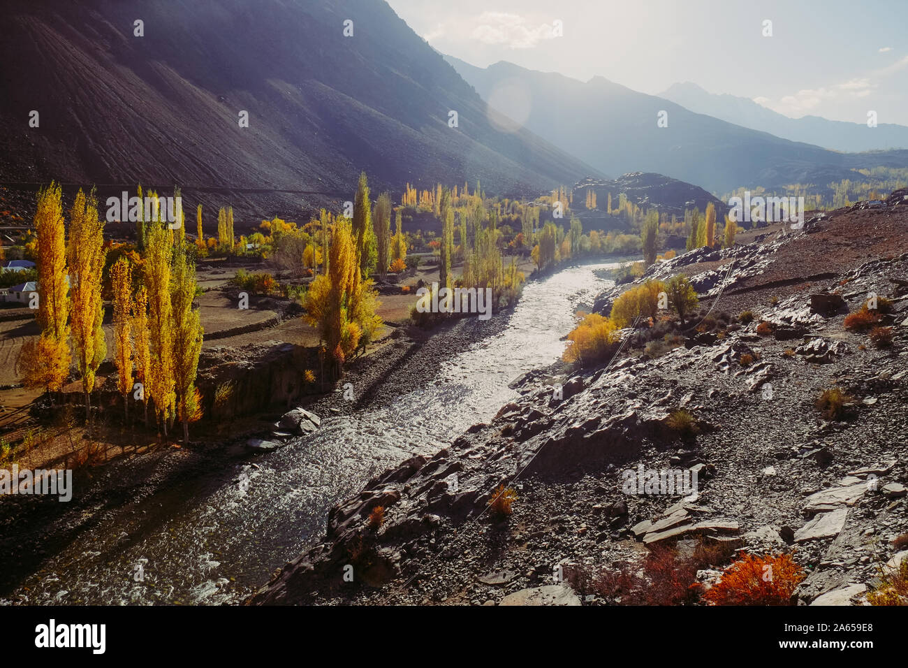 Morning sunlight shining on Gupis valley. Beautiful landscape view of colorful trees in autumn season with shiny Gilgit river against Hindu Kush mount Stock Photo