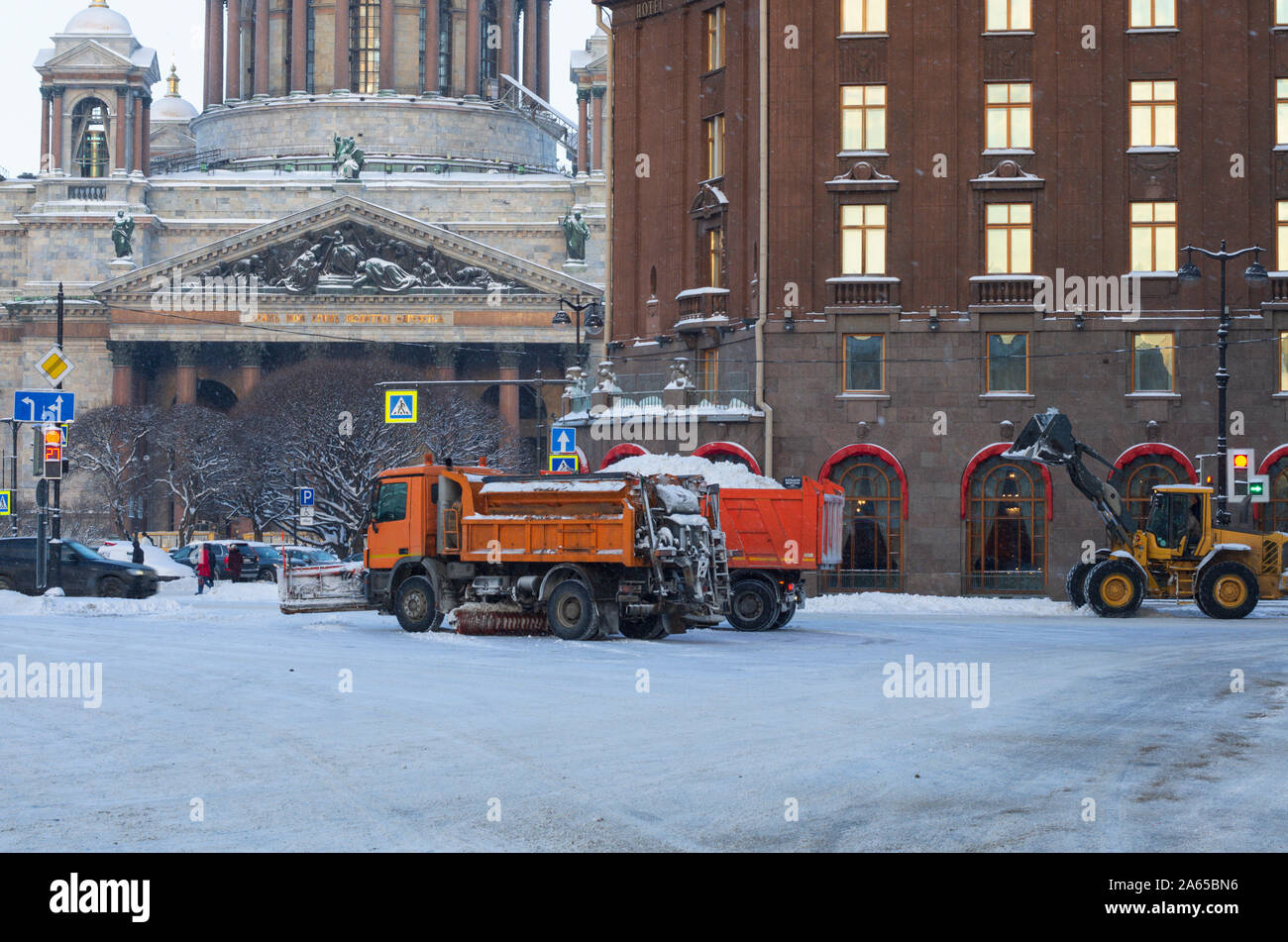 Snow removal equipment clears the city of the fallen snow in the winter morning and at a distance unidentified people (St. Petersburg, Russia) Stock Photo