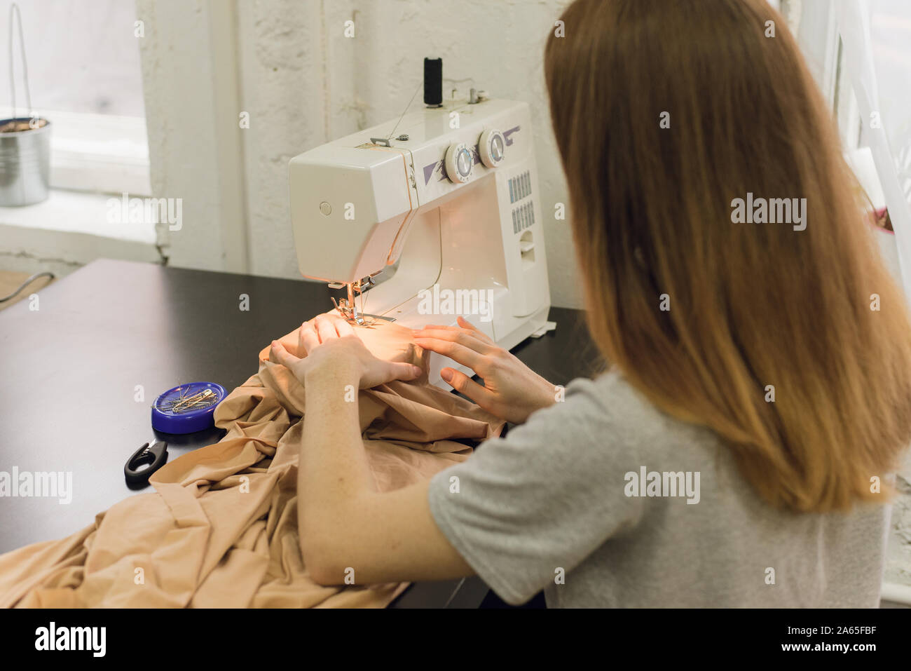 A young girl sews on a sewing machine in the Studio. Cute seamstress ...