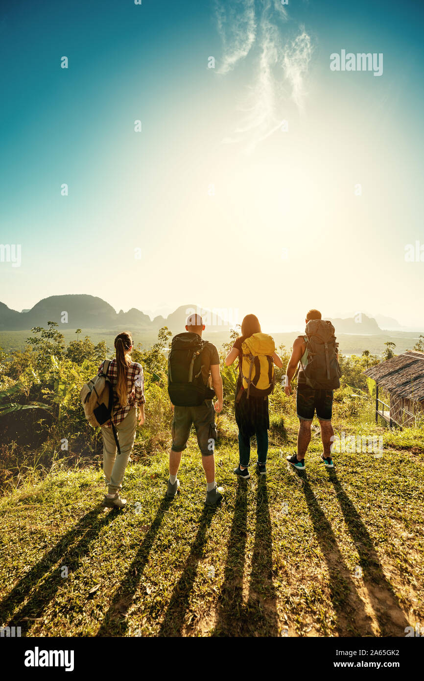 Four friends hikers and travellers stands on sunrise viewpoint on sea and islands Stock Photo