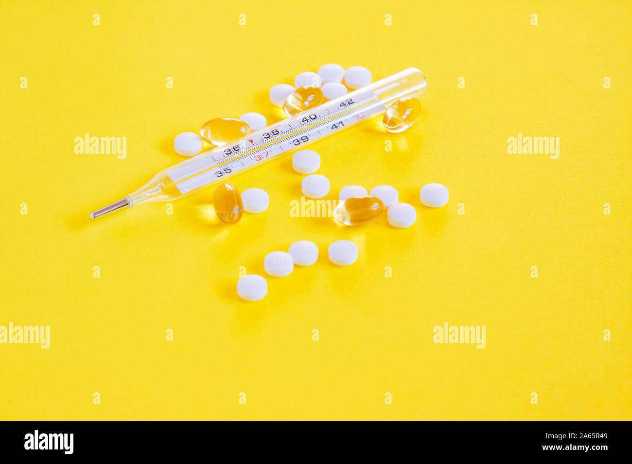 Glass mercury thermometer, white pills and capsules on yellowbackground. Fever heat, antipyretic tablets, cold. Medicine concept Stock Photo