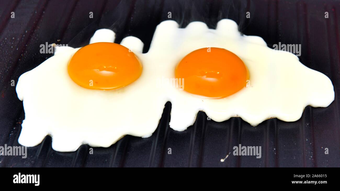 Two eggs frying on a griddle pan Stock Photo Alamy