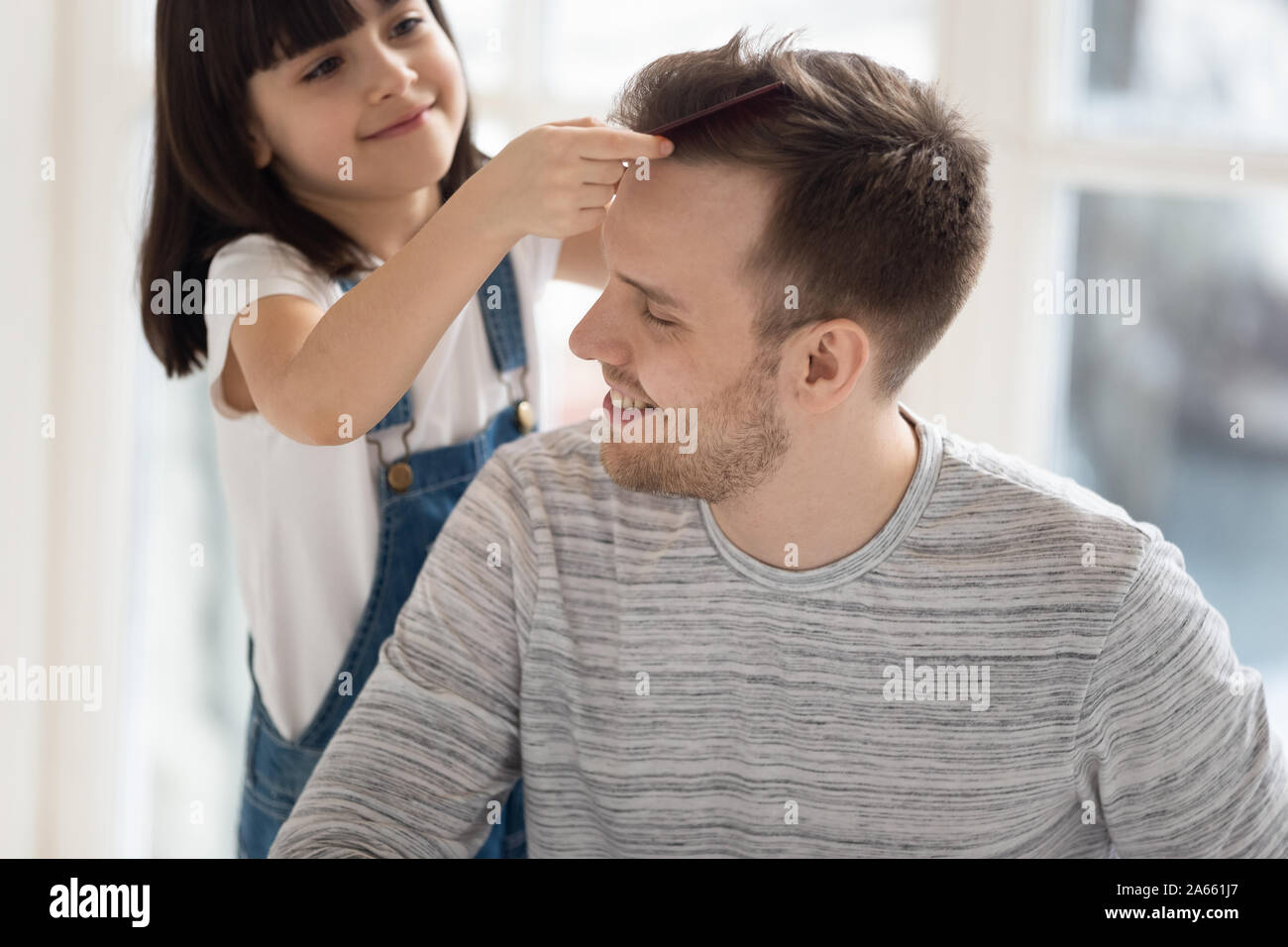 Little preschool cute daughter combing fathers hair. Stock Photo
