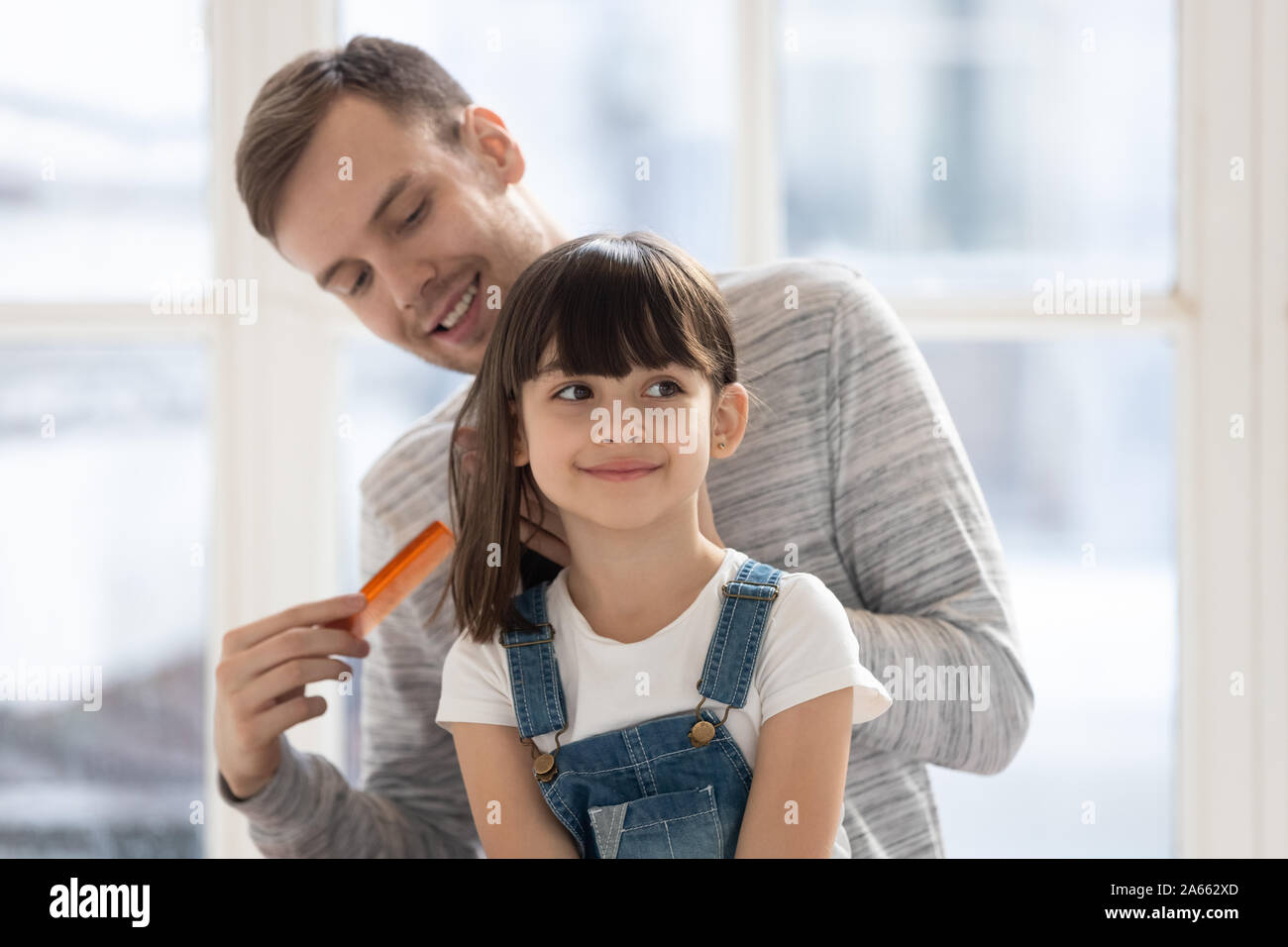 Happy millennial single father combing hair of daughter. Stock Photo