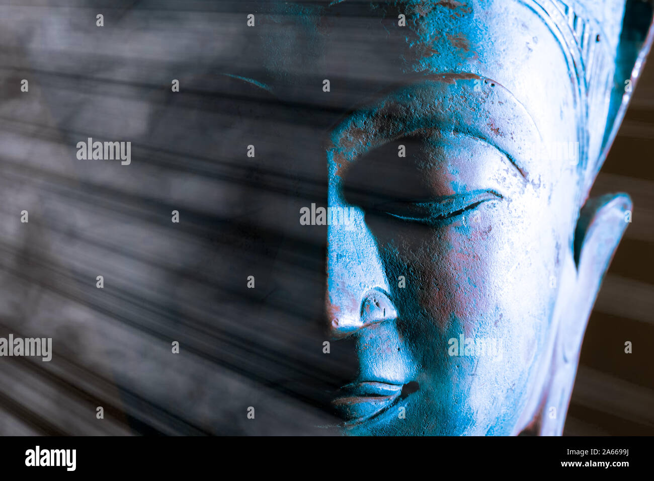 Buddha face close-up. Spiritual enlightenment. Zen Buddhism. Traditional Thai statue with ethereal light. Peaceful blue tone meditation image. Awakeni Stock Photo