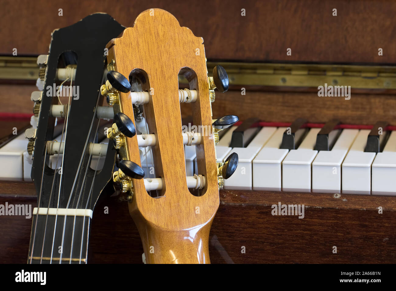 Music practice room. Acoustic guitar headstock and piano close-up. Two classical guitars resting on an old piano. Musical instruments in close up. Stock Photo