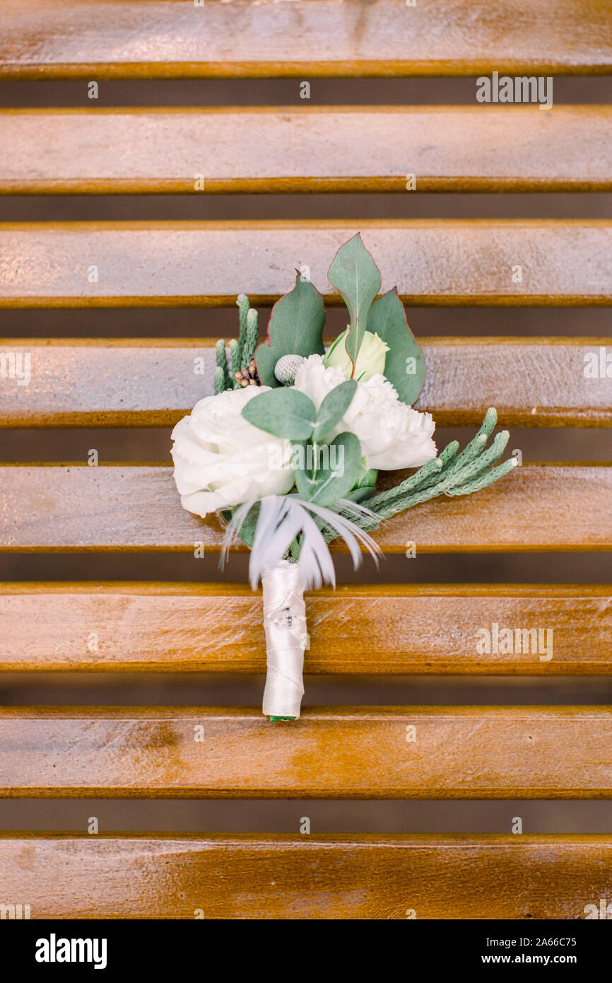 White flowers and greenery boutonniere on wooden rustic chair. Wedding accessory for groom. Stock Photo