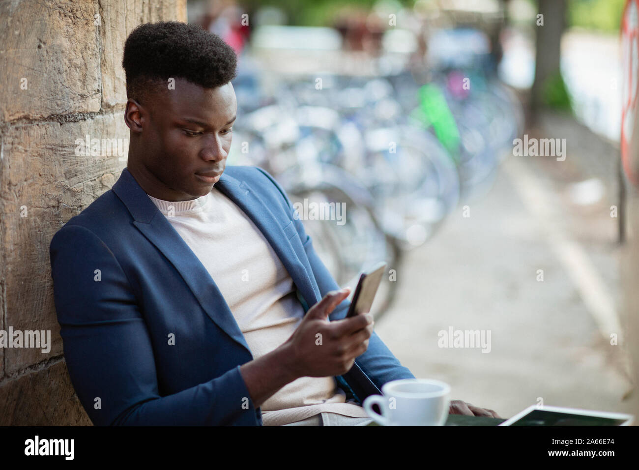 Businessman sitting down at an outdoor table in a city while typing on his mobile phone. Stock Photo