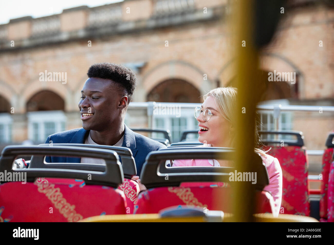 A male and female co-worker taking the bus home from work together, they are smiling while looking at the view. Stock Photo