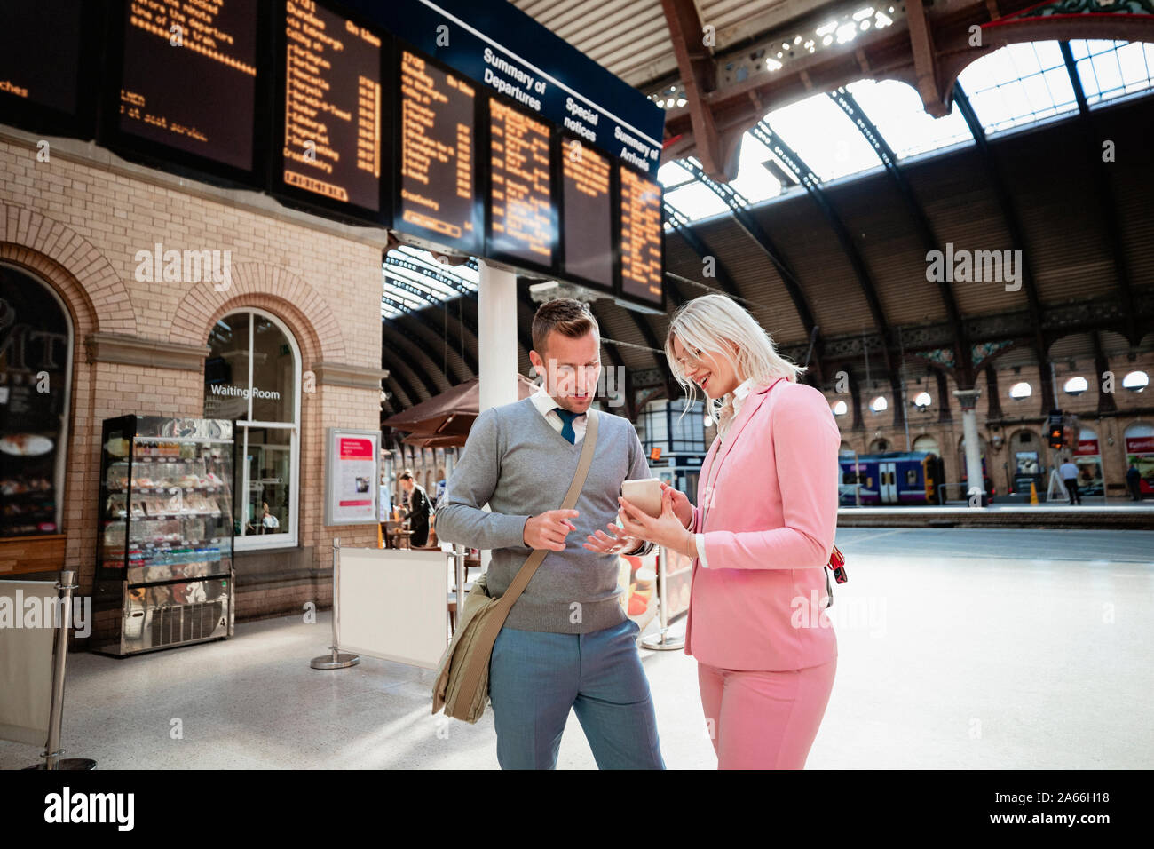A businessman and businesswoman standing together at a train station. The woman is showing the man something on her mobile phone. Stock Photo