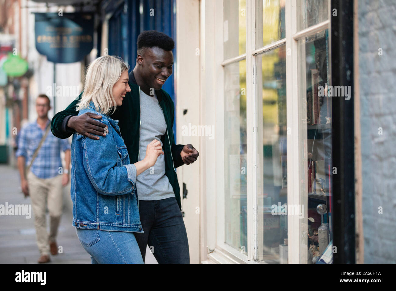 A man and woman standing outside a shop window together, he has his arm around her. Stock Photo