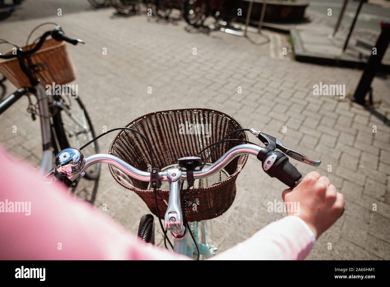 Over the shoulder view of a woman riding a bicycle. The main focus is on the front of the bicycle and its basket. Stock Photo
