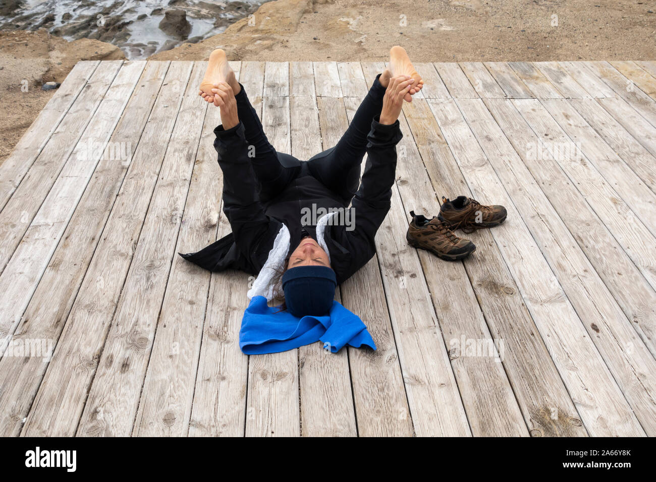 Mature Spanish woman stretching, performing Yoga on beach boardwalk