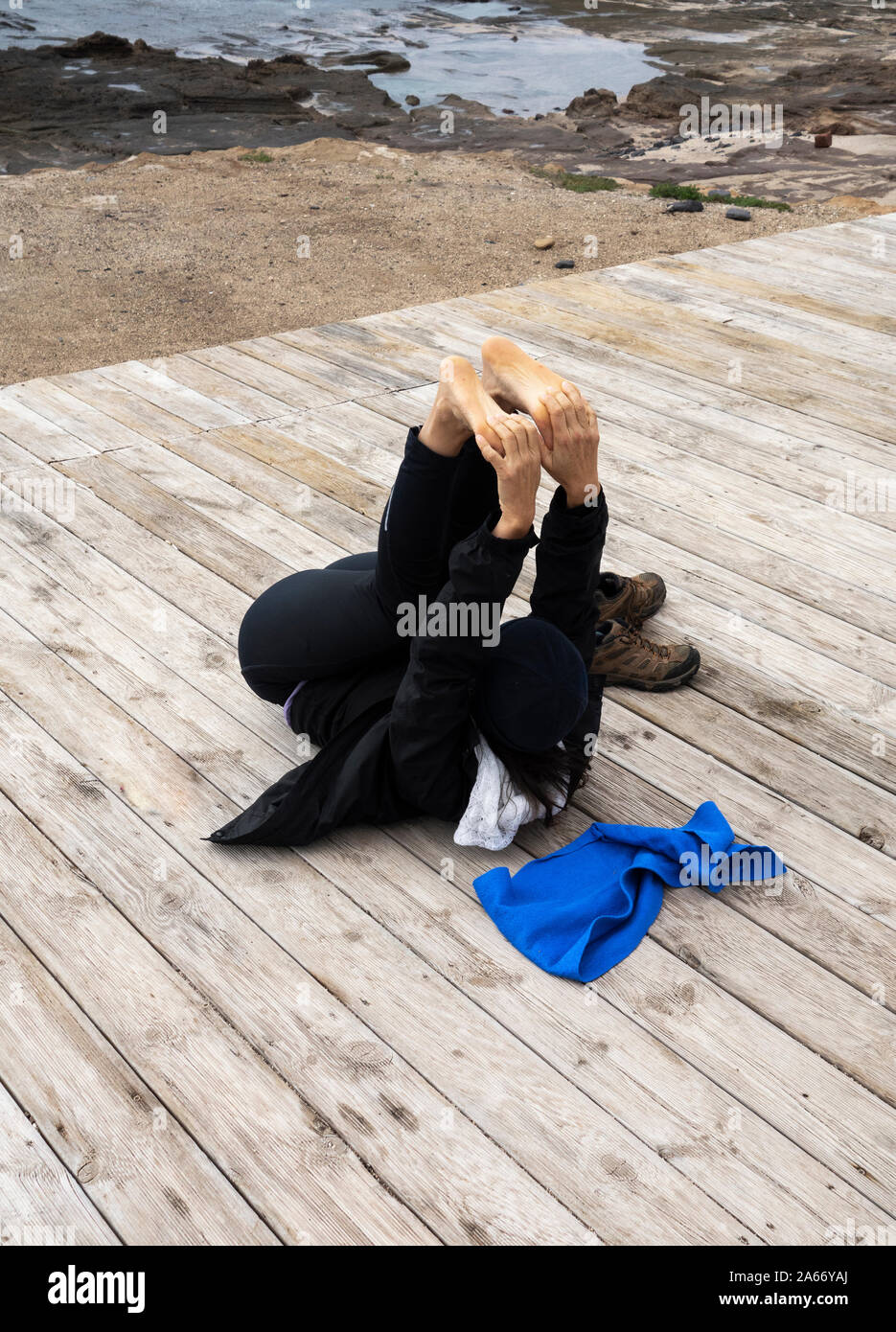 Mature Spanish woman stretching, performing Yoga on beach boardwalk