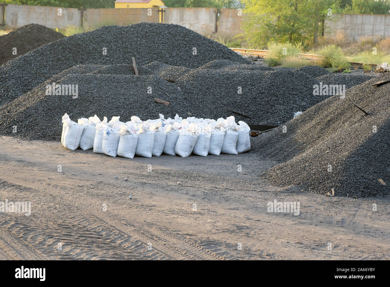 On the ground are mountains of black coal. White full bags with black charcoal. Coal warehouse