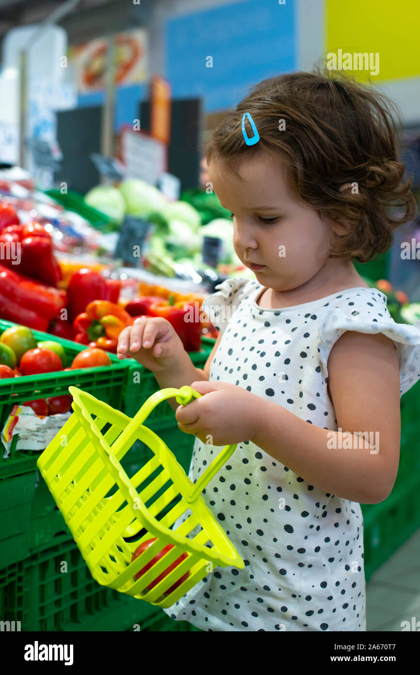 Little girl buying tomatoes in supermarket. Child hold small basket in supermarket and select vegetables. Concept for healthy eating for children. Stock Photo