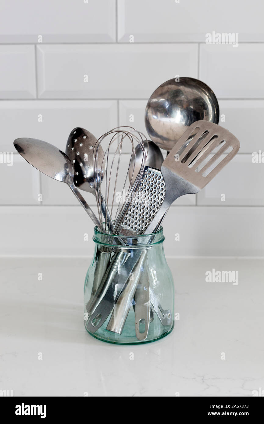 Glass container holding various stainless steel kitchen utensils Stock Photo