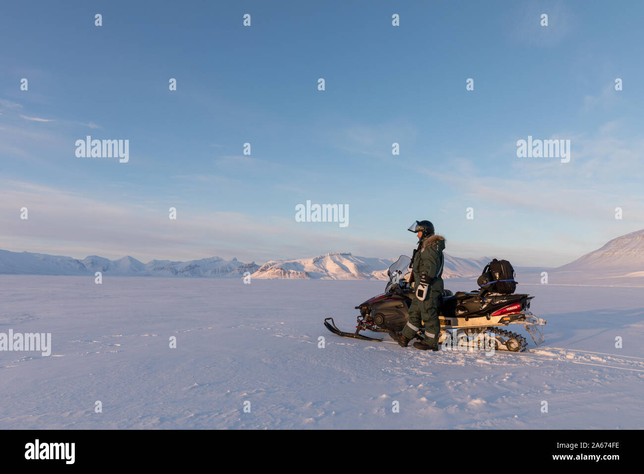 Svalbard, Norway - March 2019: Man standing next to a Yamaha snowmobile in arctic landscape at Svalbard Stock Photo