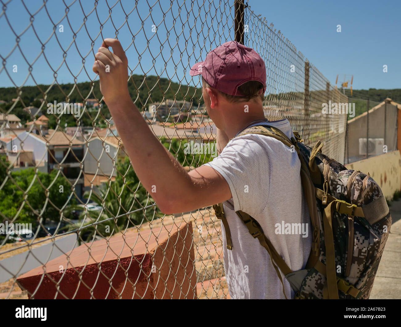 A tourist man with a backpack stands at the metal fence behind which the city is located. Stock Photo