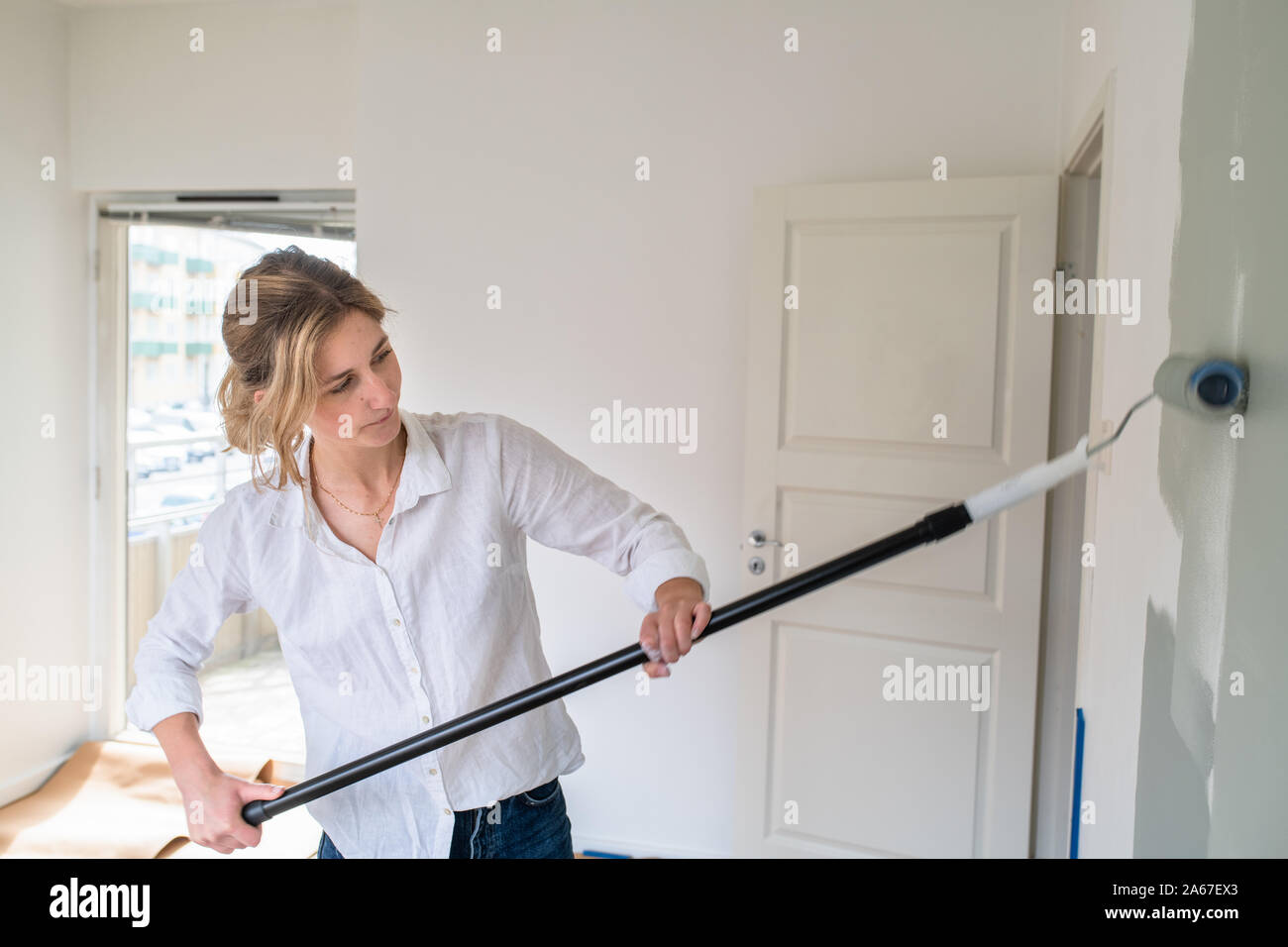 Woman rolling gray paint onto wall Stock Photo Alamy