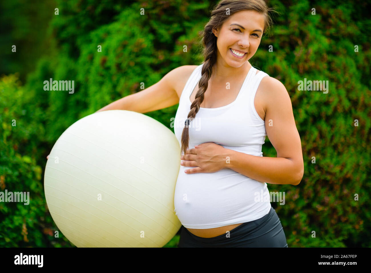 Portrait Of Pregnant Woman Touching Abdomen While Holding Fitness Ball Stock Photo