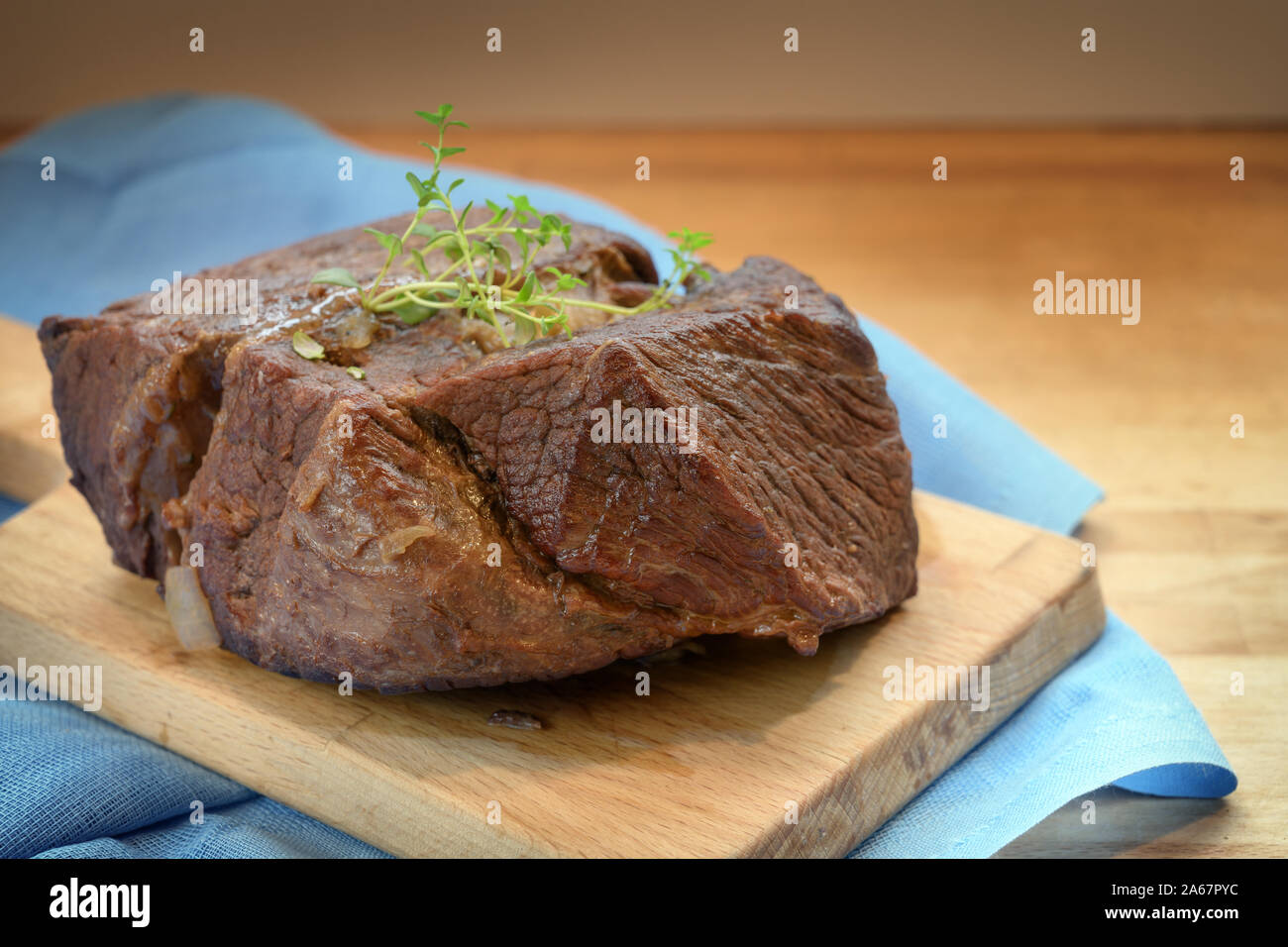 Braised roast beef with thyme garnish on a wooden board and a blue napkin for a festive dinner like boeuf bourguignon, copy space, selected focus, nar Stock Photo