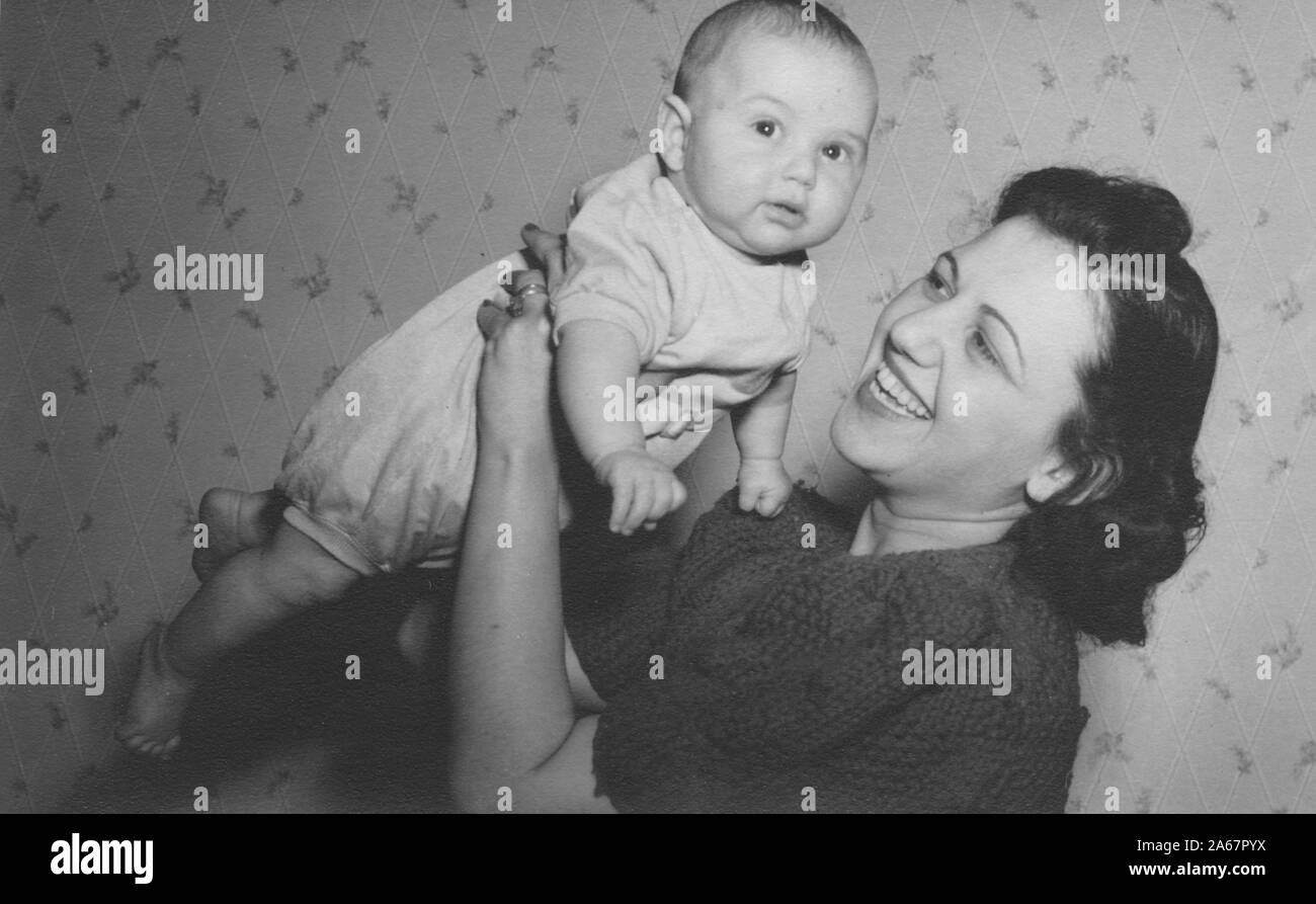 A young Jewish-American mother smiles as she lifts her baby into the air in a suburban living room in New York City, New York, 1940. () Stock Photo