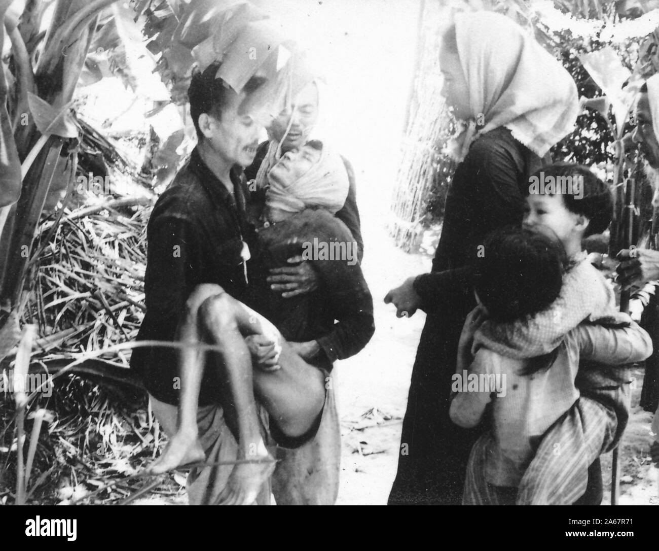 Vietnamese refugees stand in the jungle during the Vietnam War, with children and apparent casualties, 1975. () Stock Photo