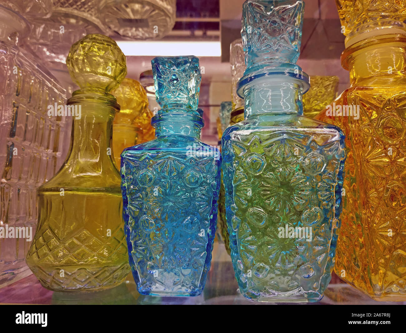 Glass decanters on a store shelf. Yellow and blue glass decanters of various shapes are sold. Bar equipment. Stock Photo