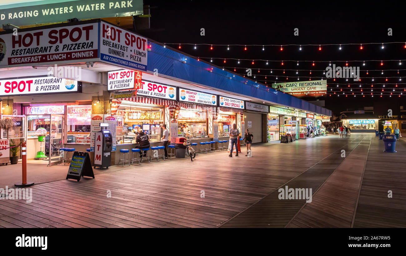 A small number of people walk and visit stores and game rooms on an almost empty ocean boardwalk at night when summer is over. Stock Photo