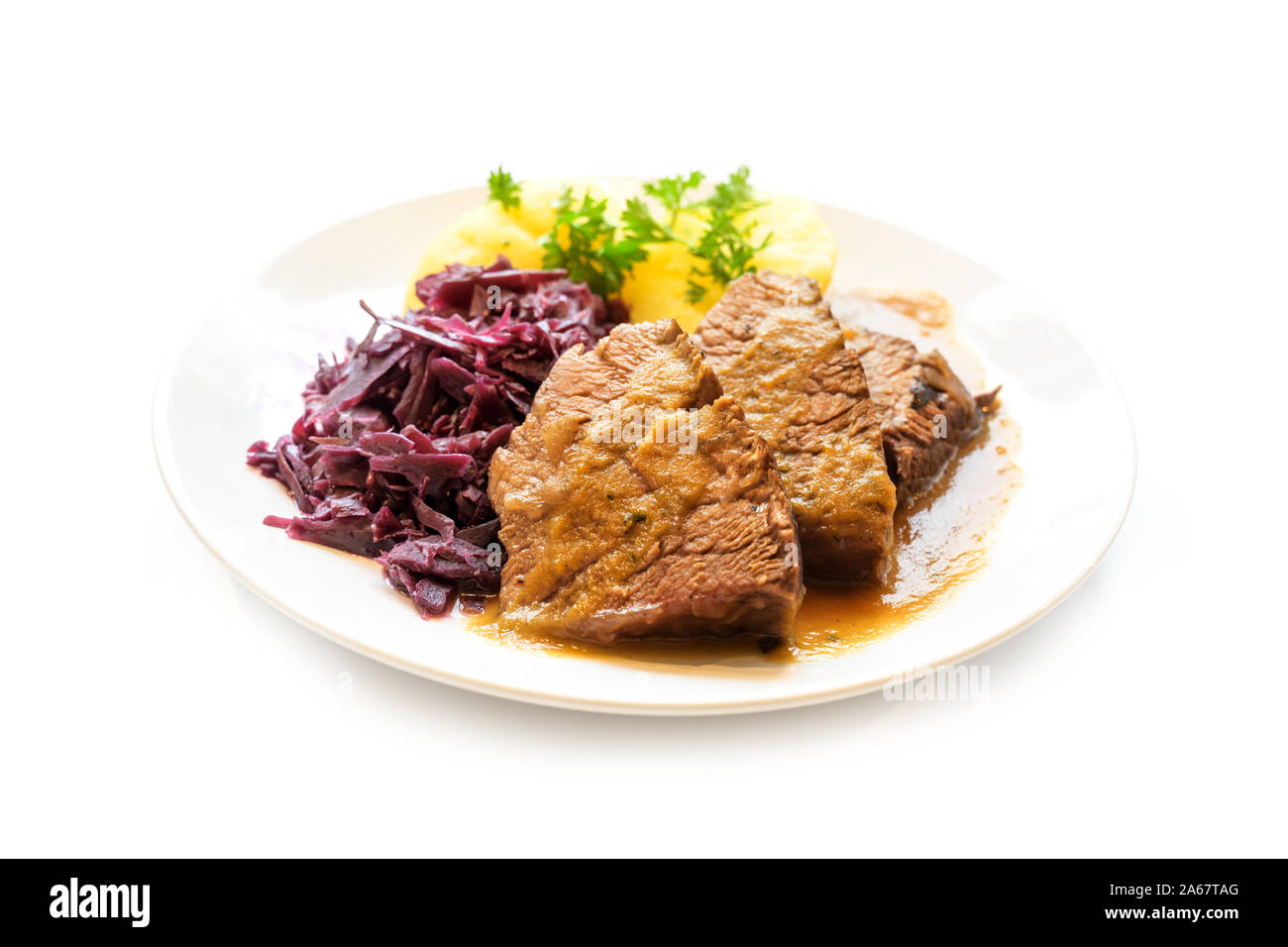 braised beef with potatoes, red cabbage and parsley garnish on a plate, isolated on a white background, selected focus, very narrow depth of field Stock Photo