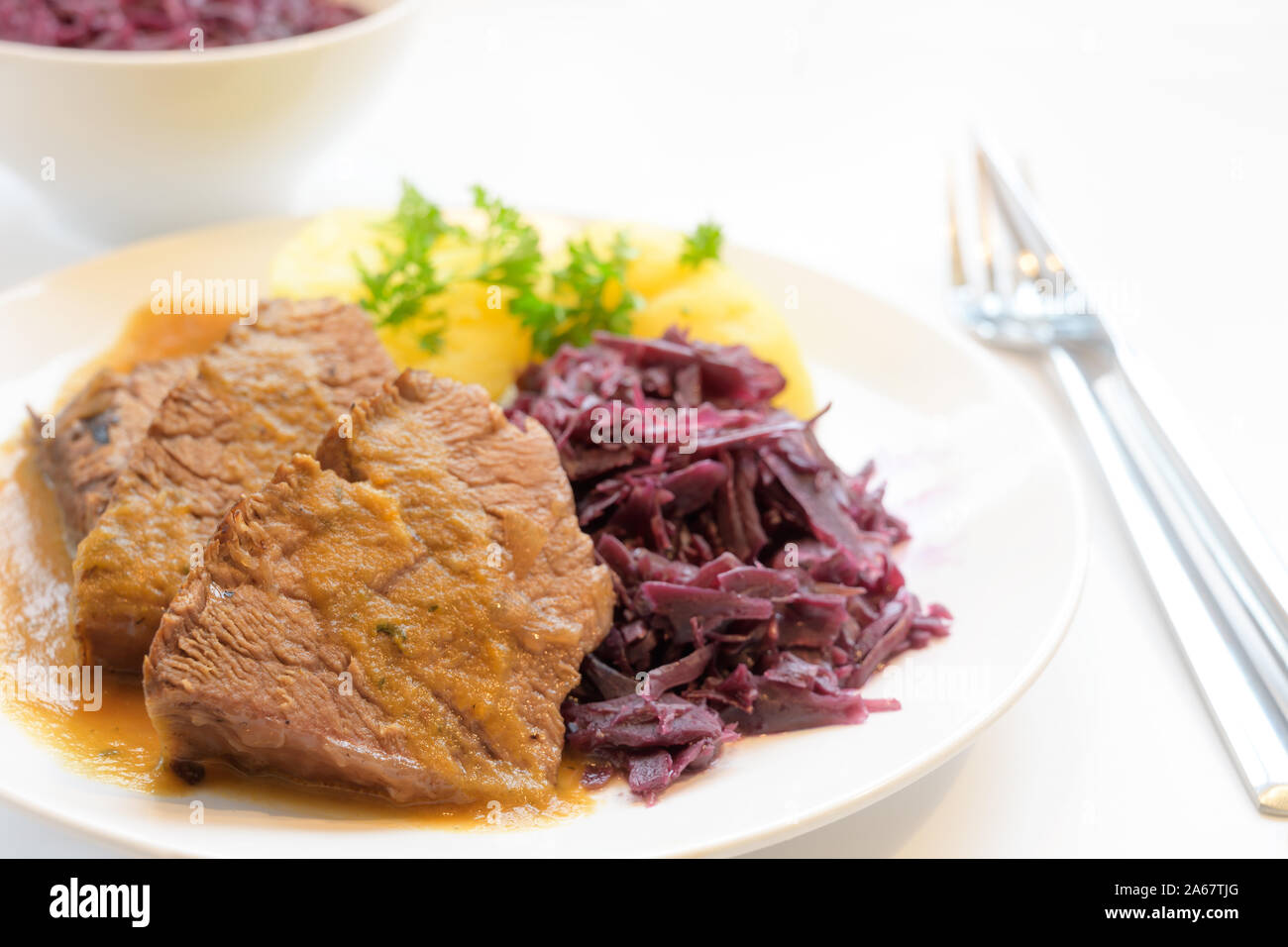 braised beef with potatoes, red cabbage and parsley garnish, served on a plate on a white table, copy space, selected focus, very narrow depth of fiel Stock Photo