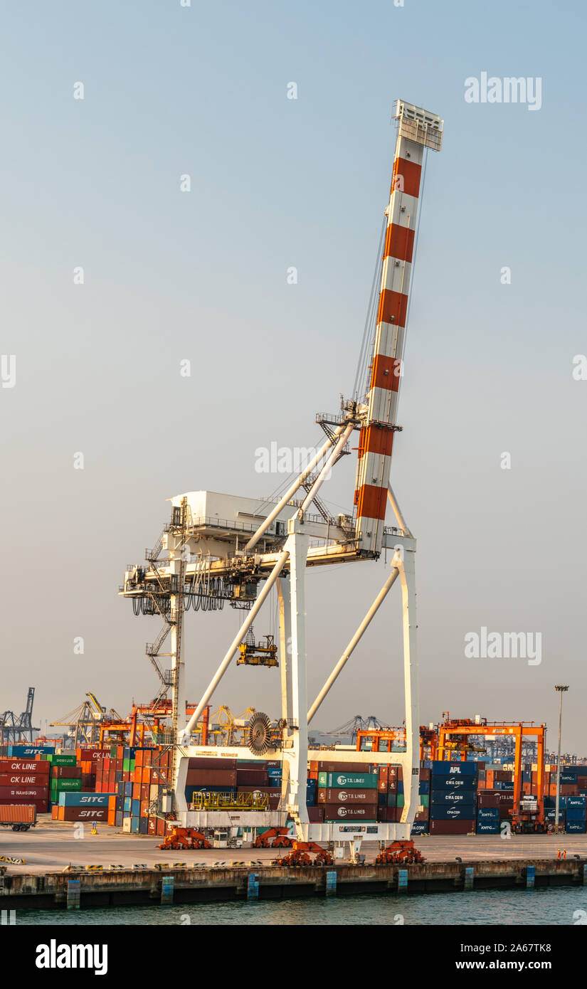 Laem Chabang seaport, Thailand - March 17, 2019: Tall non-working red and white container crane against light blue evening sky. Plenty of colorful box Stock Photo
