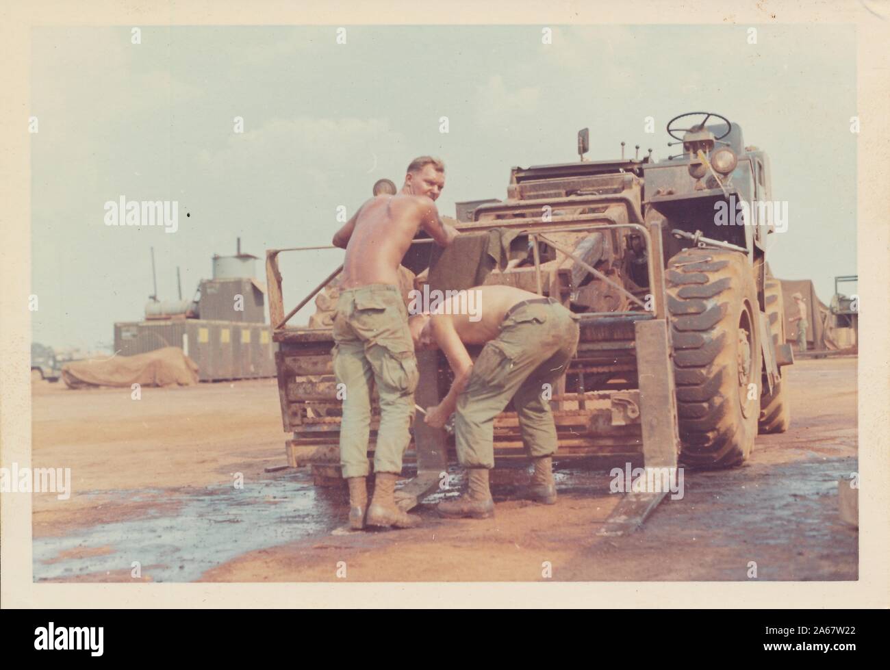 Several shirtless American servicemen look over their shoulders as they work on a military forklift in Vietnam during the Vietnam War, 1970. () Stock Photo
