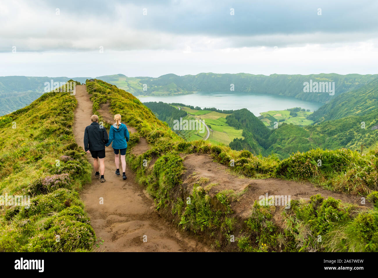 A young couple holding hands while walking towards the Grota do Inferno viewpoint at Sete Cidades on Sao Miguel Island, Azores. Stock Photo