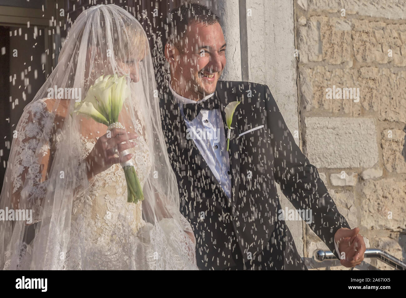 FAŽANA, CROATIA - OCTOBER 12, 2019: Unidentified smiling newlyweds on their way out of the church after the wedding ceremony, with the shower of under Stock Photo