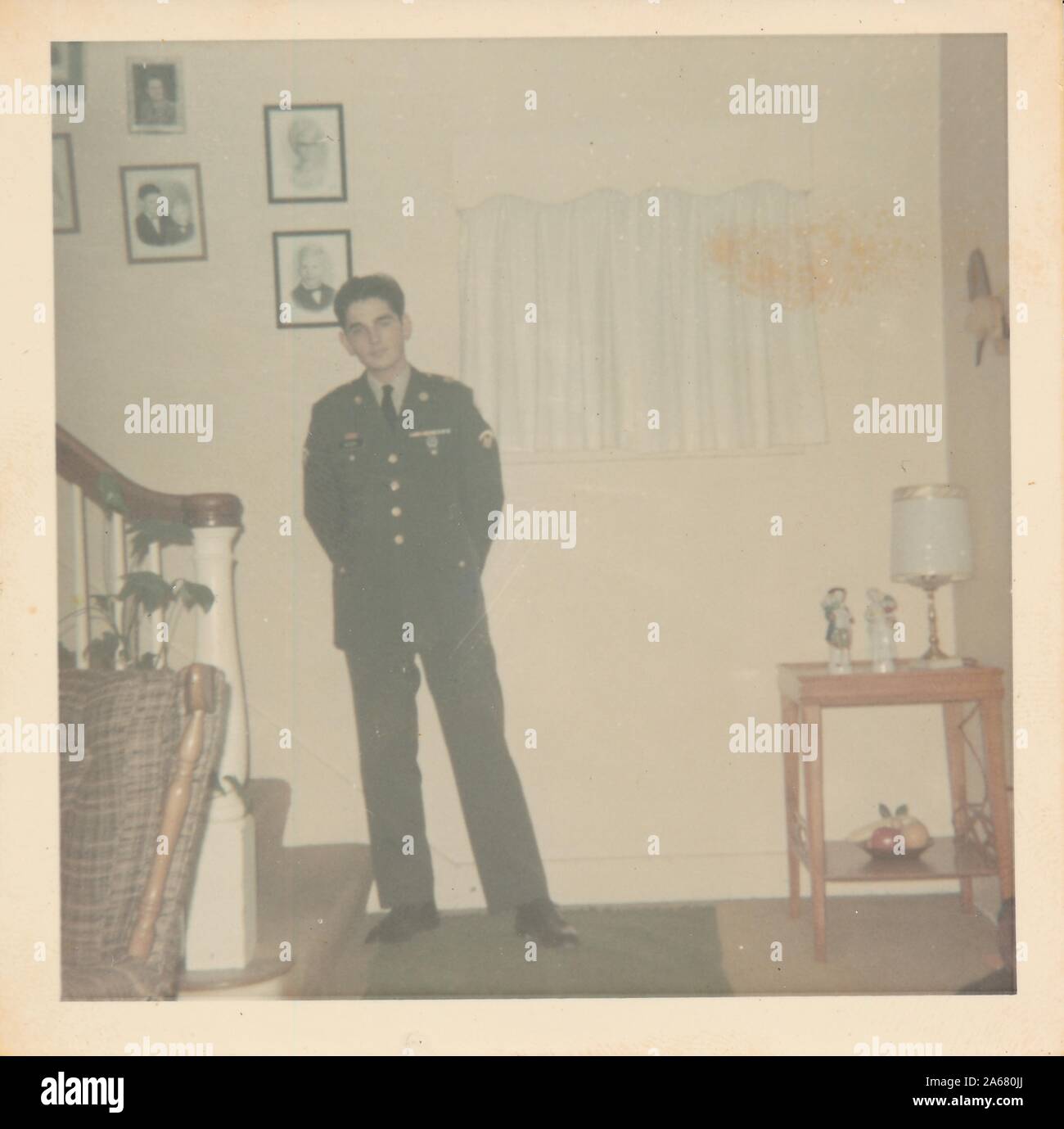 Full-length shot of a uniformed serviceman, facing the camera, standing at the base of a stairway in a suburban living room, United States of America, 1965. () Stock Photo