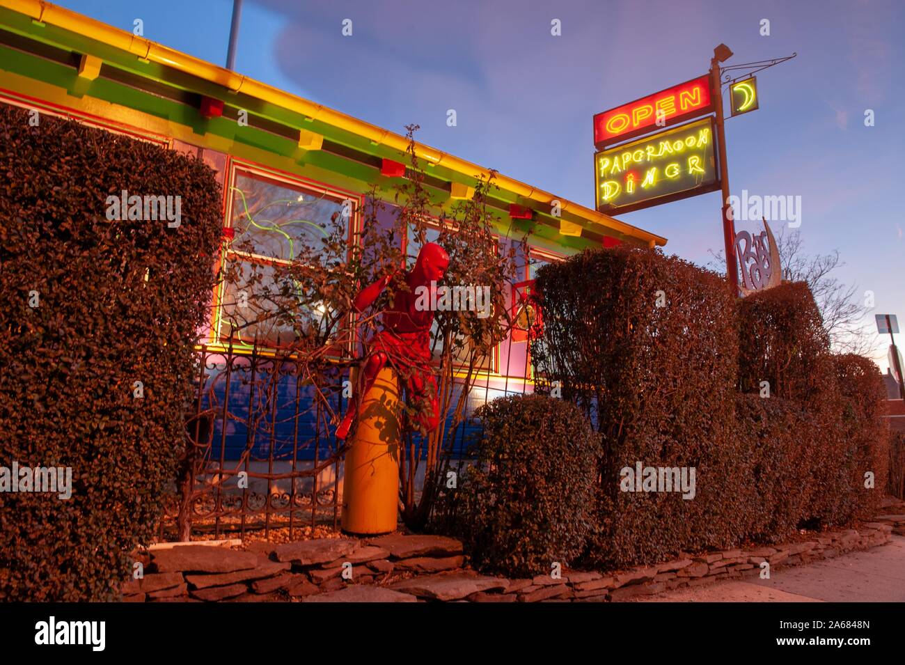 Low-angle evening shot of manicured hedges, vines wrapping around a red statue, and a neon sign outside the coloful exterior of the Papermoon Diner, Baltimore, Maryland, January 8, 2008. From the Homewood Photography Collection. () Stock Photo