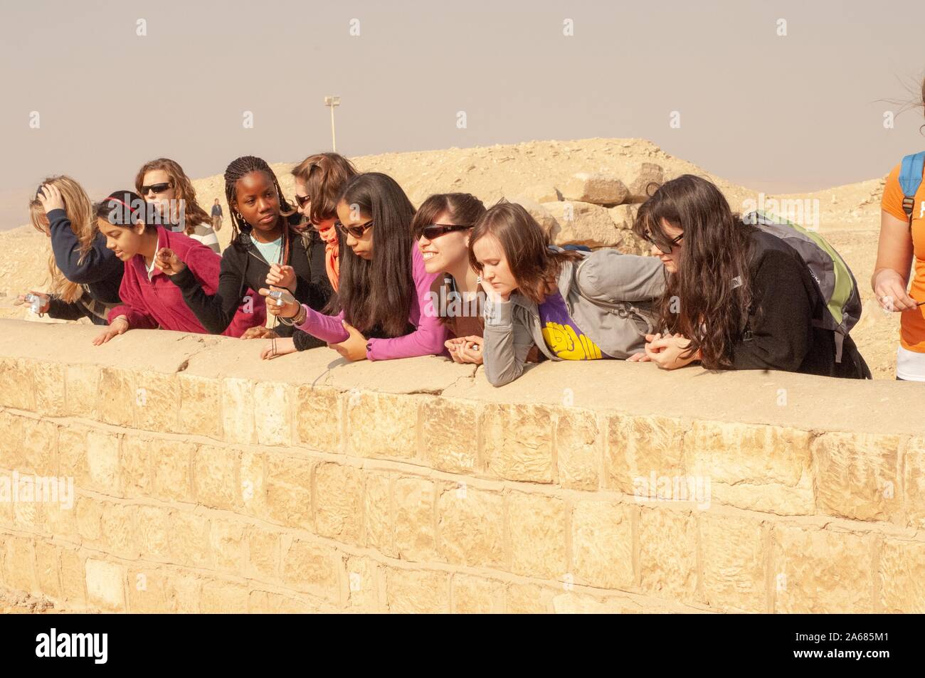 A row of Johns Hopkins University students, outside on a sunny day, chatting and leaning forward to look over a low stone wall, Giza, Egypt during a study abroad program, January 6, 2008. From the Homewood Photography Collection. () Stock Photo