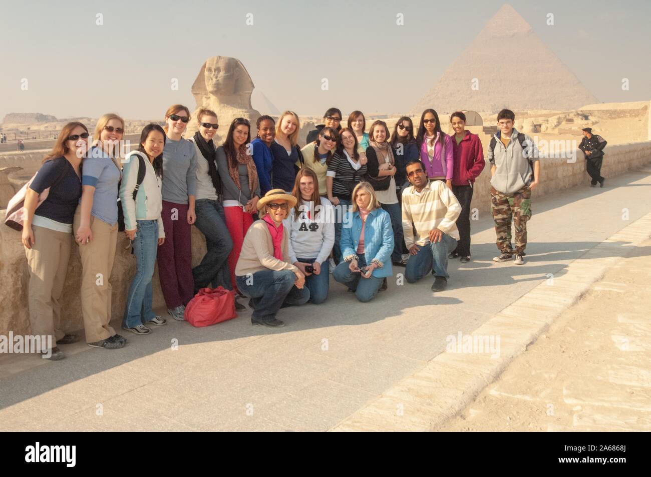 Egyptologist Betsy Bryan poses with a row of Johns Hopkins University students, outside on a sunny day, with a low stone wall, and with the Sphinx and a pyramid visible in the background, Giza, Egypt during a study abroad program, January 7, 2008. From the Homewood Photography Collection. () Stock Photo