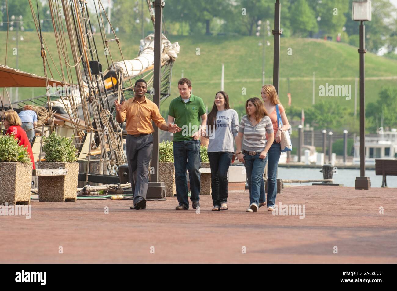 Johns Hopkins University students, on a sunny day, walking on a brick wharf next to a historic ship docked in the Inner Harbor area, Baltimore, Maryland, May, 2008. From the Homewood Photography Collection. () Stock Photo