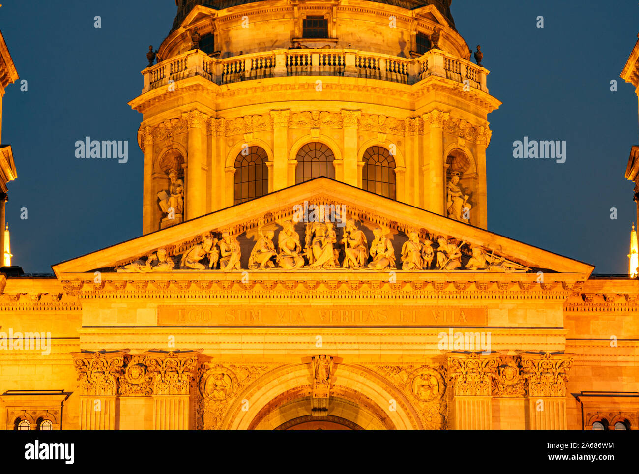 Triangular tympanum of the St. Stephen's Basilica facade, decorated with christian themed statues lit by yellow light after sunset, Budapest, Hungary. Stock Photo
