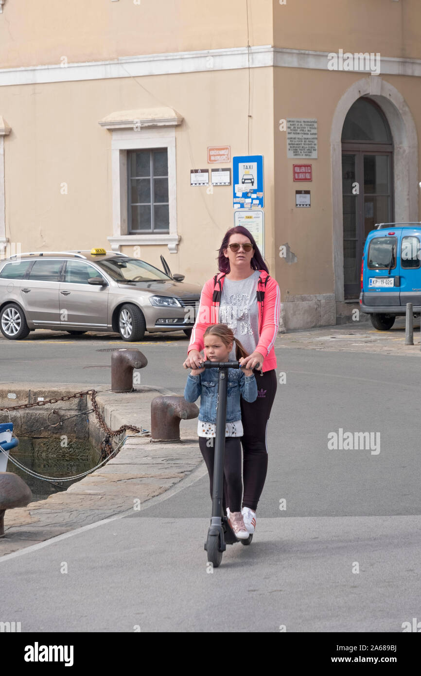 A mother & daughter ride an electric scooter along the Adriatic coastline in Piran, Slovenia. Stock Photo