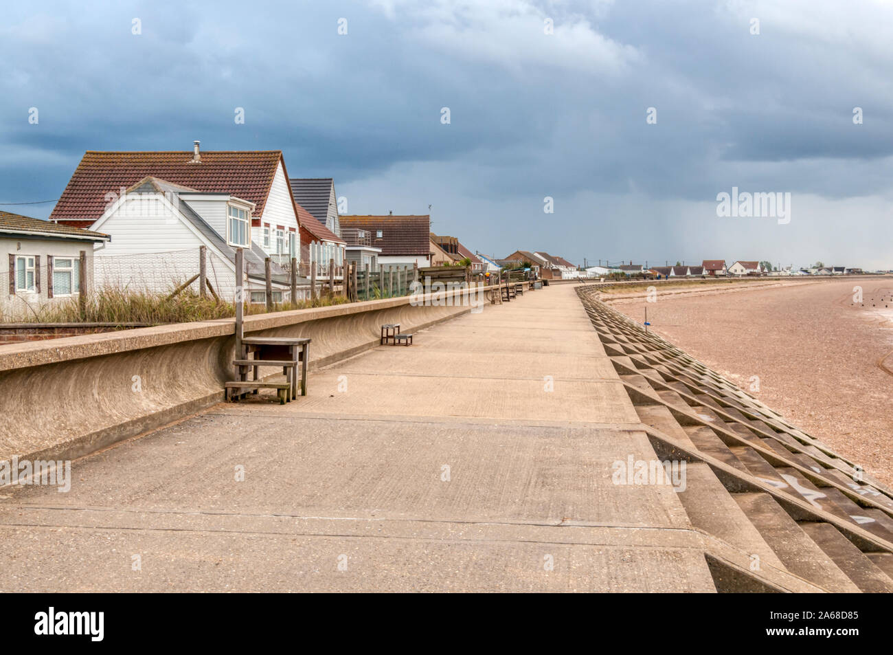 Protective sea wall to avoid flooding in front of seaside bungalows facing The Wash at Heacham in West Norfolk. With storm clouds gathering. Stock Photo