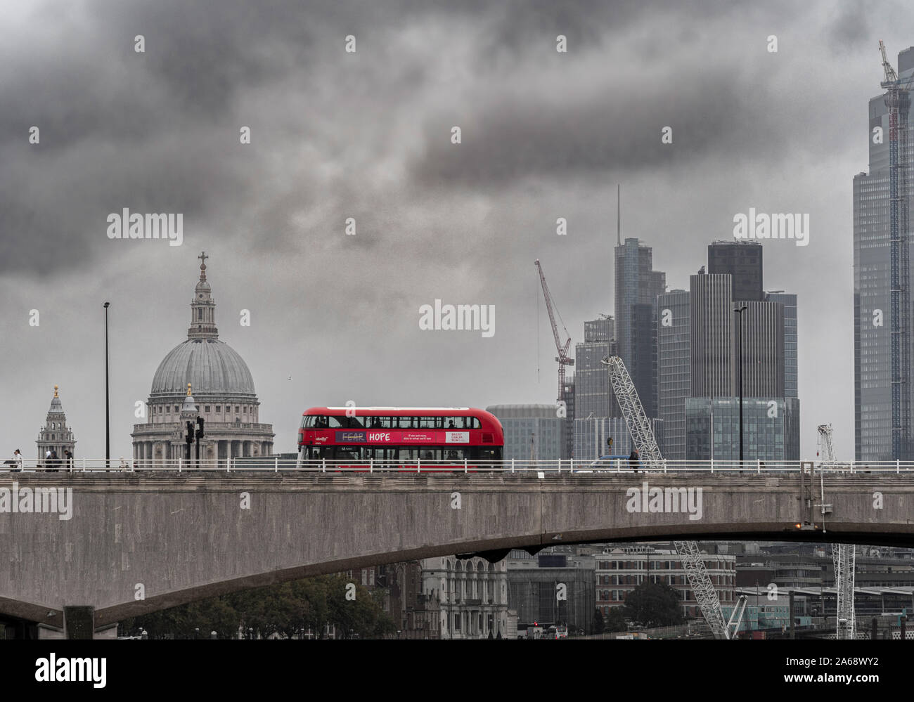 Waterloo Bridge over the river Thames on a grey misty day with a red double decker London bus passing over. St Pauls, and City of London office buildi Stock Photo