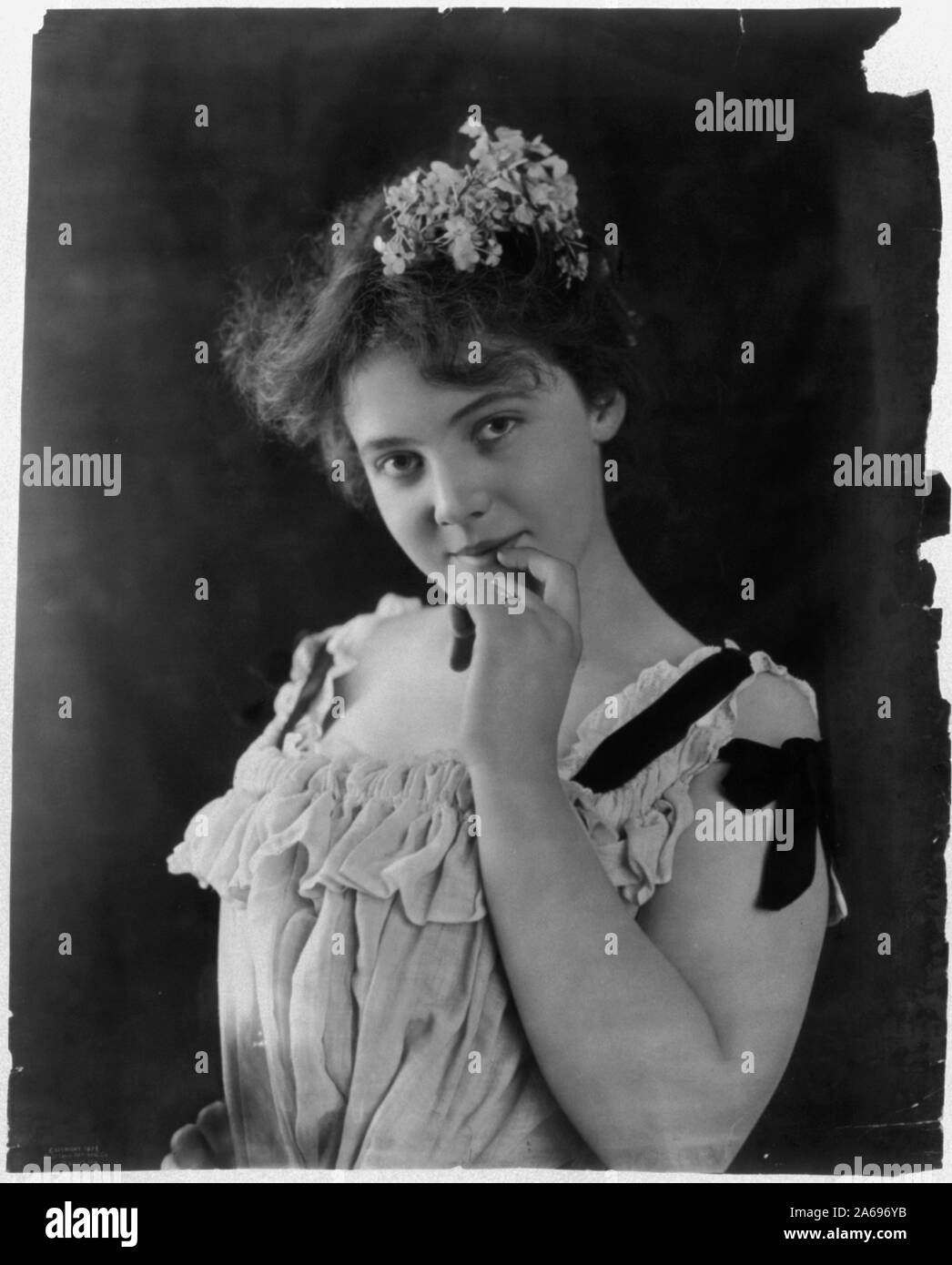Young woman, half lgth., with flowers in her hair, holding left hand to chin Stock Photo