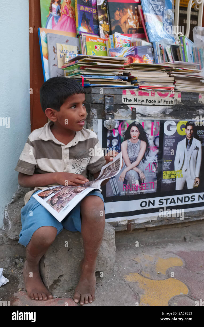 A young Indian boy sits by a news stall in Mumbai, India, leafing through a magazine Stock Photo