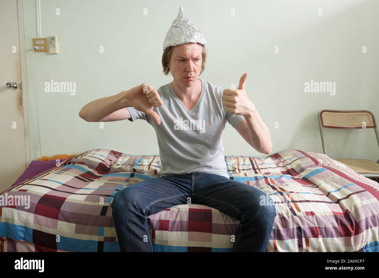 Confused young man with tin foil hat making decision in the bedroom Stock Photo
