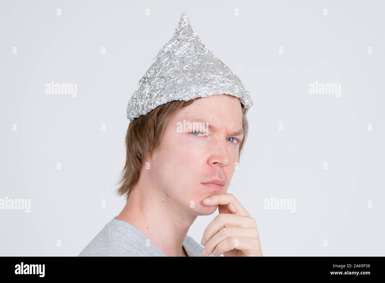 Closeup profile view of young man with tinfoil hat thinking and looking at camera Stock Photo